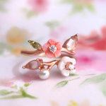A rose gold Sakura Symphony Ring adorned with peridot, freshwater pearl, rose quartz, hand-carved shell flowers, and sparkling moissanite accents, capturing the essence of spring blossoms.