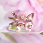 A rose gold Sakura Symphony Ring adorned with peridot, freshwater pearl, rose quartz, hand-carved shell flowers, and sparkling moissanite accents, capturing the essence of spring blossoms.