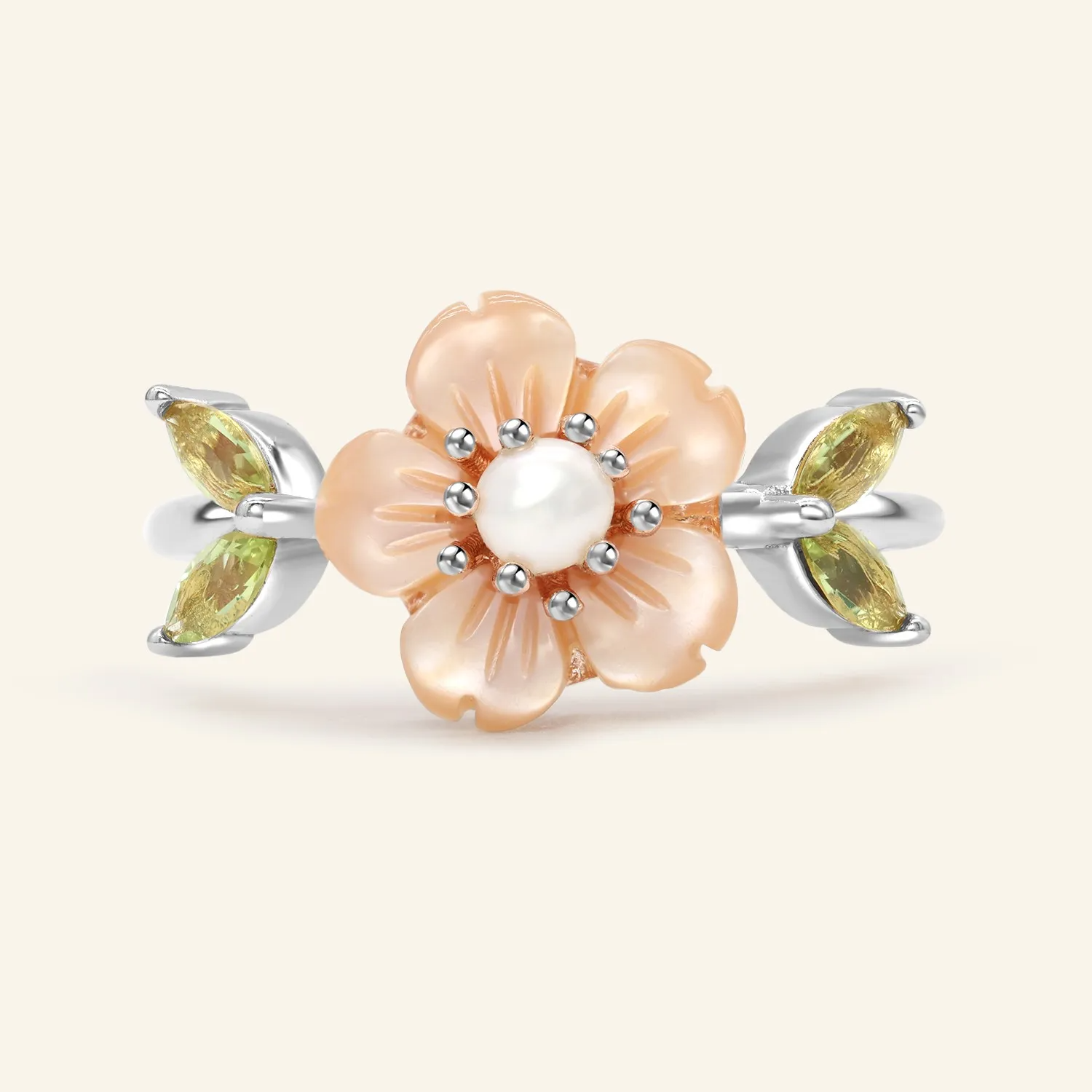 A delicate sakura blossom ring in silver featuring a central freshwater pearl, surrounded by hand-carved shell petals resembling cherry blossoms, with peridot stones set as the leaves on either side.
