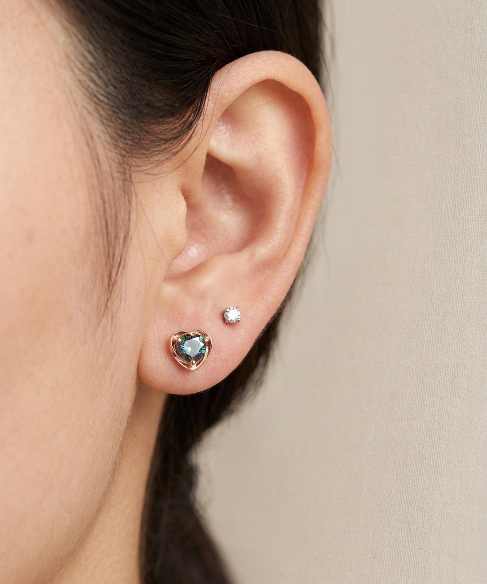 Ear stack featuring 18k rose gold Sculpted Heart Nest Moissanite Stud in Celestial Teal alongside a clear accent stud.