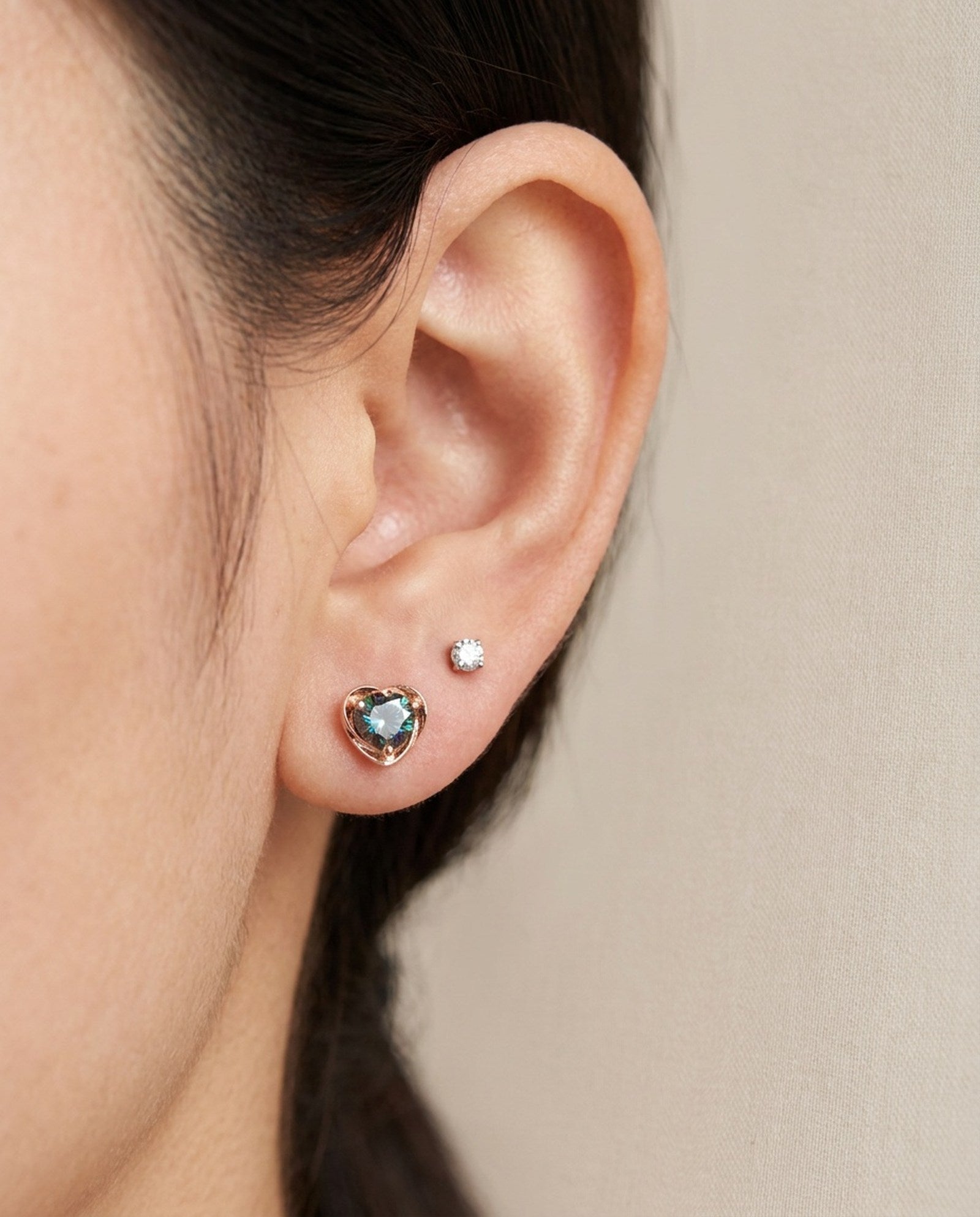 Ear stack featuring 18k rose gold Sculpted Heart Nest Moissanite Stud in Celestial Teal alongside a clear accent stud.