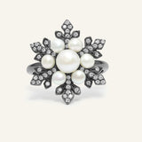 Snowflake Pearl Halo Ring in black gold, resting on a warm linen background