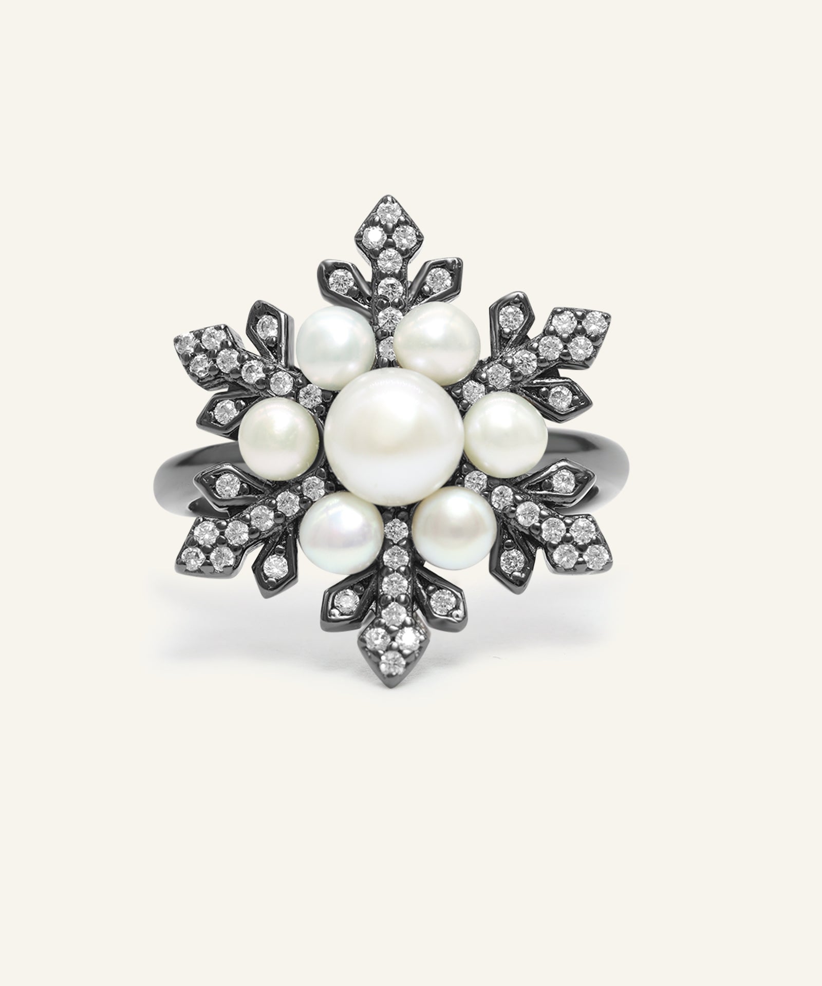 Snowflake Pearl Halo Ring in black gold, resting on a warm linen background