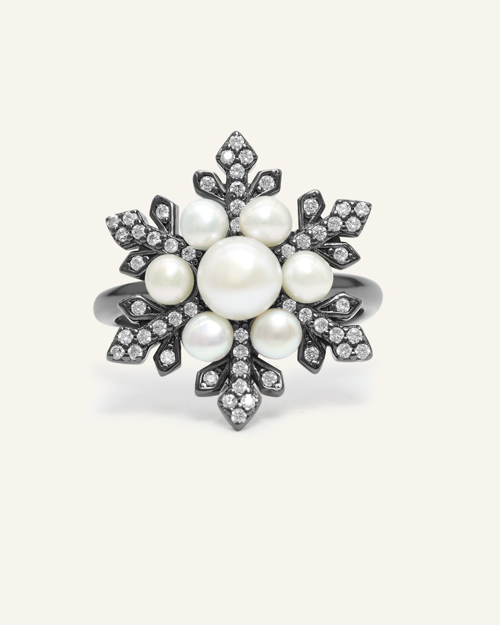 Snowflake Pearl Halo Ring in black gold, resting on a warm linen background