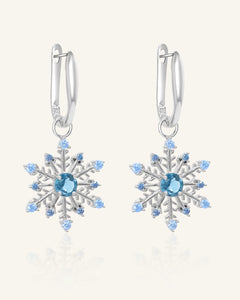 Close-up of the Snowflake London Blue Topaz Huggies in silver, resting on a warm linen background