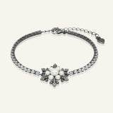 Snowflake Pearl Tennis Bracelet in black gold, resting on a warm linen background