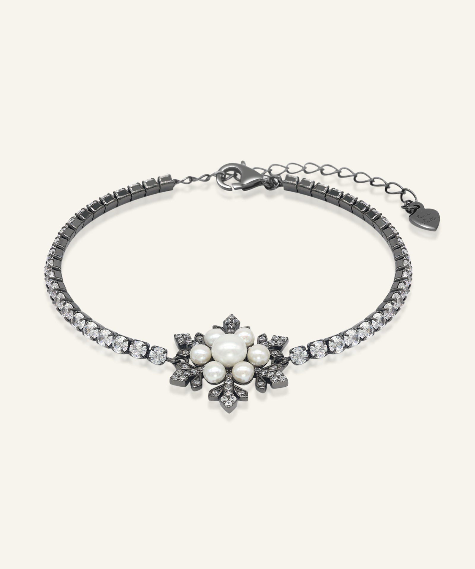 Snowflake Pearl Tennis Bracelet in black gold, resting on a warm linen background