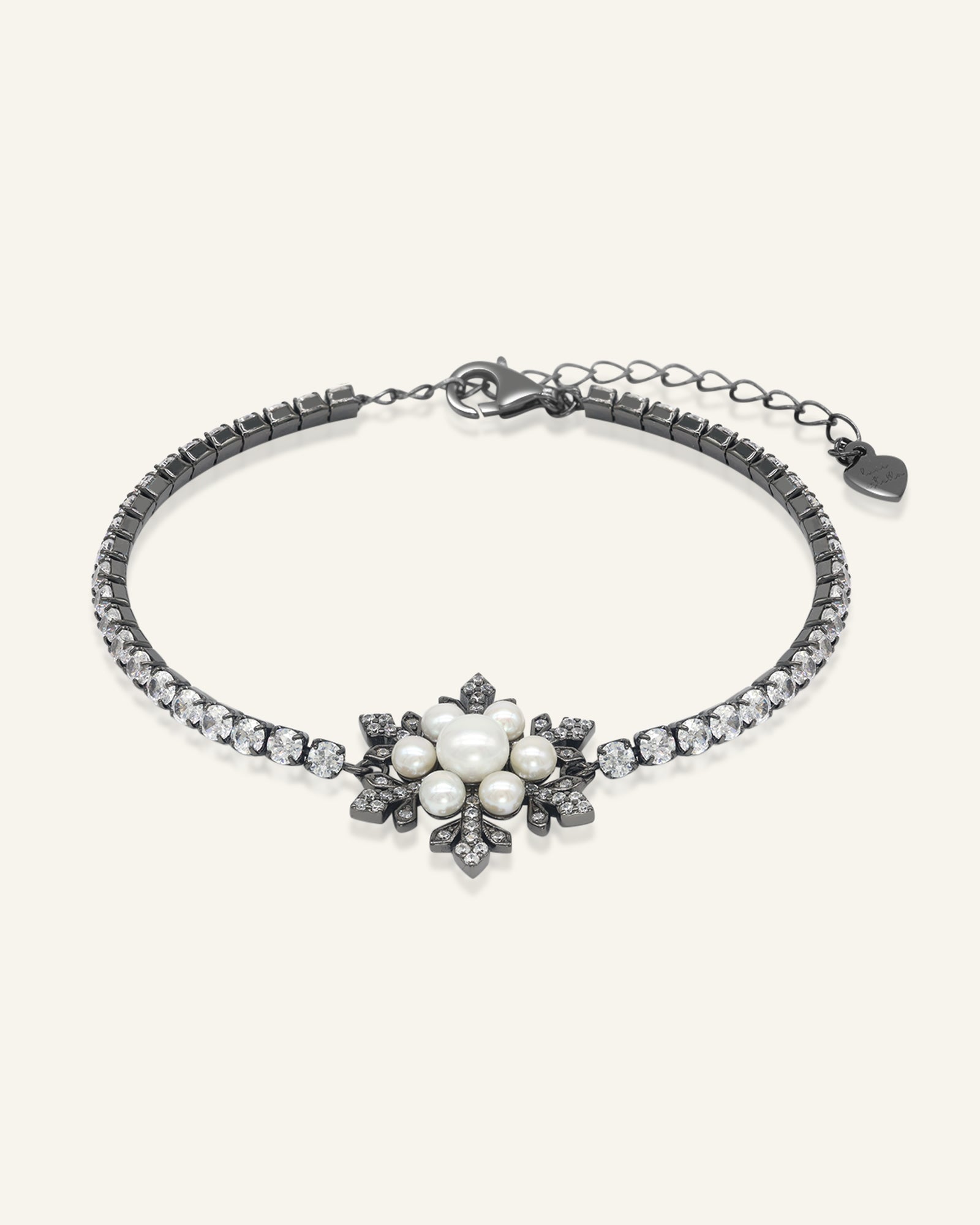 Snowflake Pearl Tennis Bracelet in black gold, resting on a warm linen background