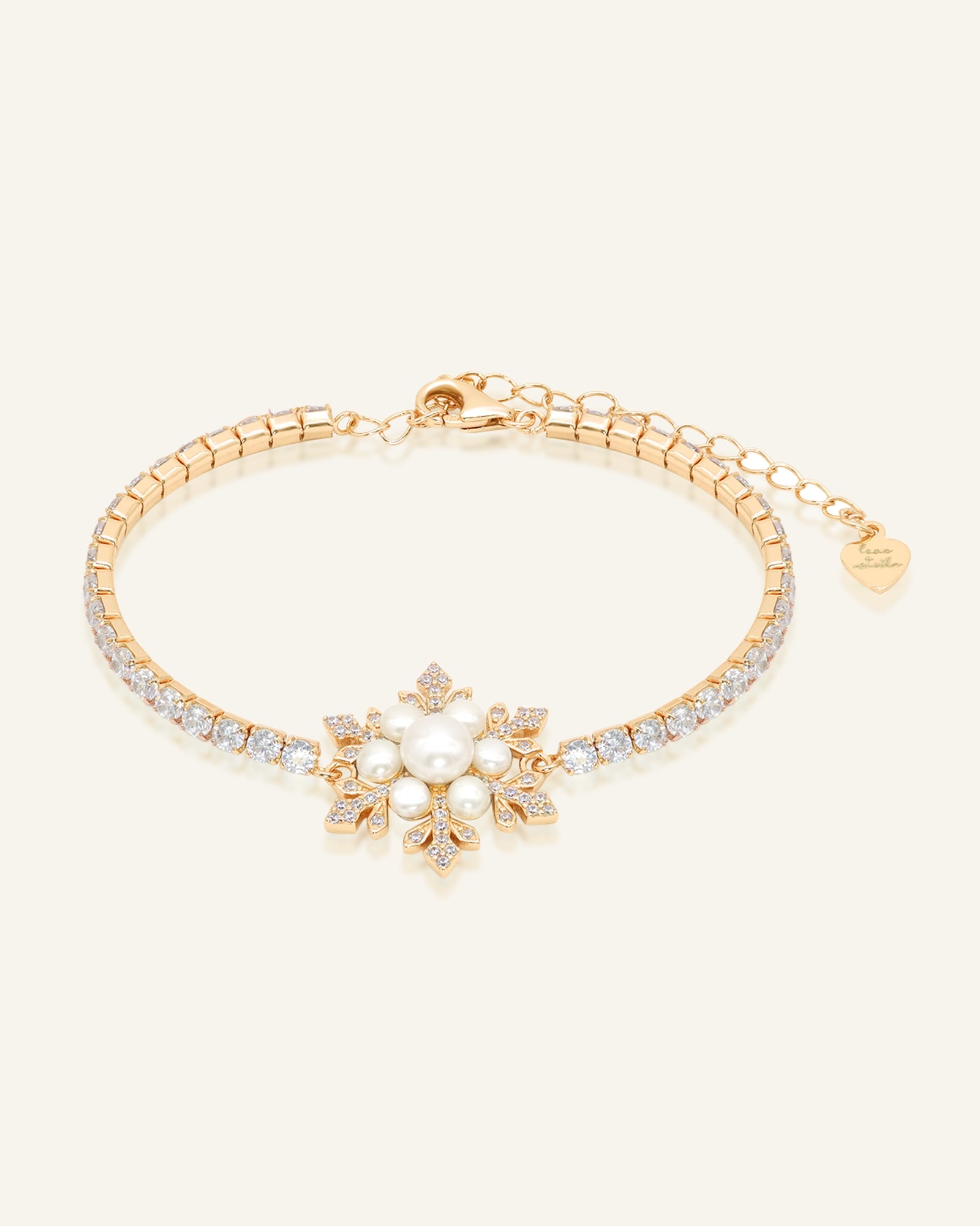 Snowflake Pearl Tennis Bracelet in yellow gold, resting on a warm linen background
