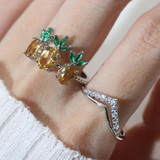 A model wearing a trio of pineapple-themed rings featuring yellow citrine gemstones mimicking the fruit's body, with green cubic zirconia leaves at the top, all set in a silver band.