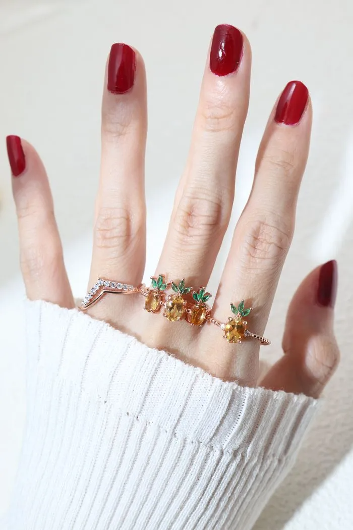 A model wearing a trio of pineapple-themed rings featuring yellow citrine gemstones mimicking the fruit's body, with green cubic zirconia leaves at the top, all set in a rose gold band.