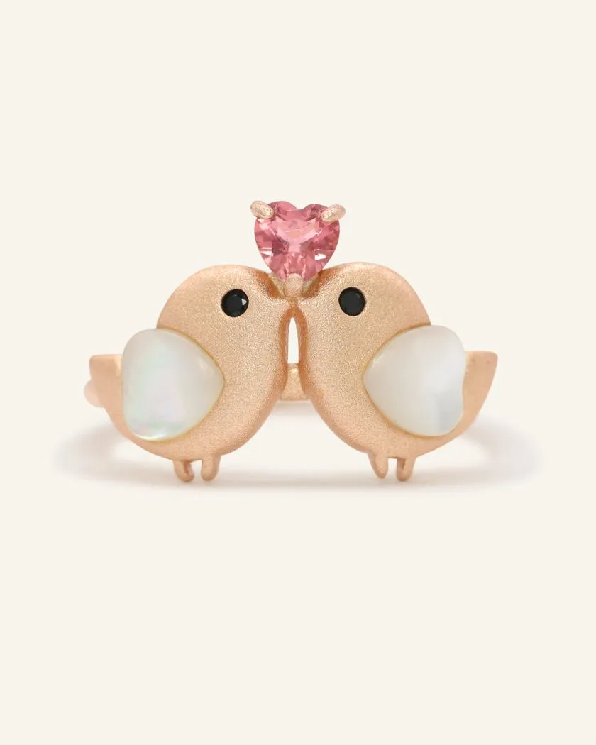 A charming rose gold ring with two birds, each with mother of pearl hearts, and a pink tourmaline heart set above them.