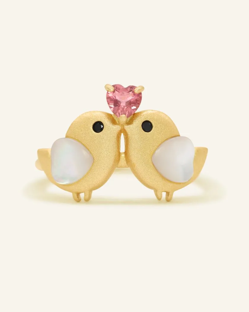 A charming yellow gold ring with two birds, each with mother of pearl hearts, and a pink tourmaline heart set above them.