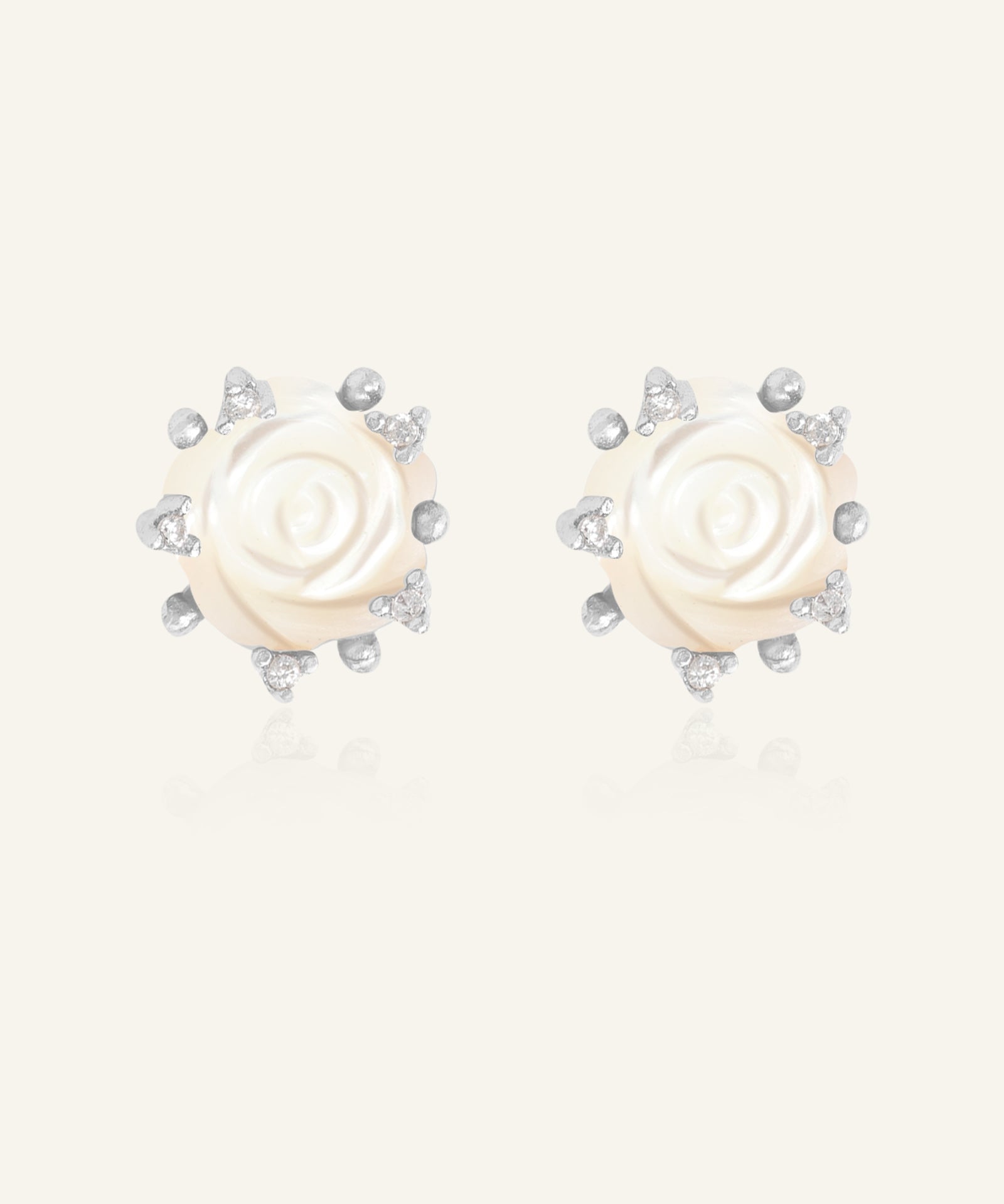 Handcarved White Shell Rose Studs in silver, resting on a warm linen background
