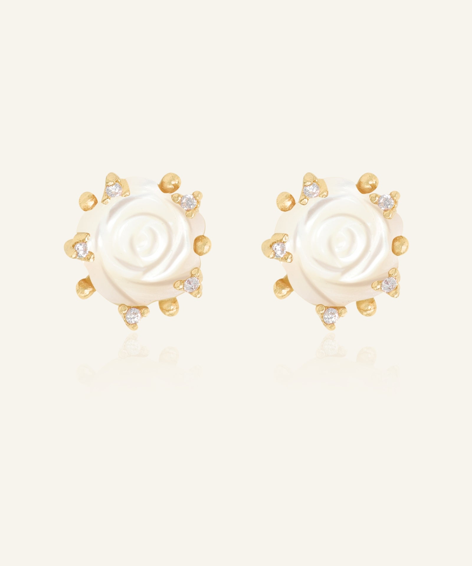 Handcarved White Shell Rose Studs in yellow gold, resting on a warm linen background