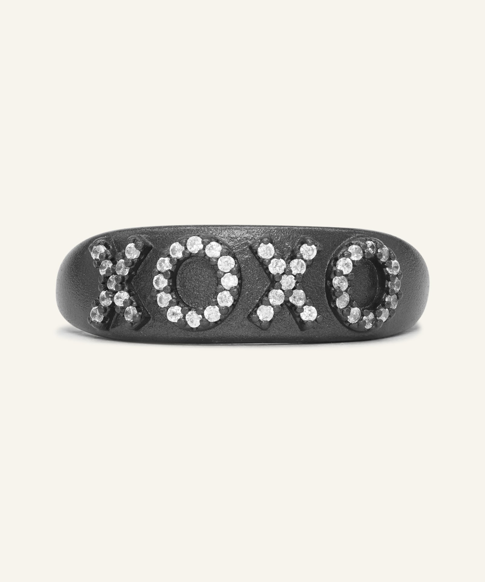 XOXO Ring in black gold, resting on a warm linen background