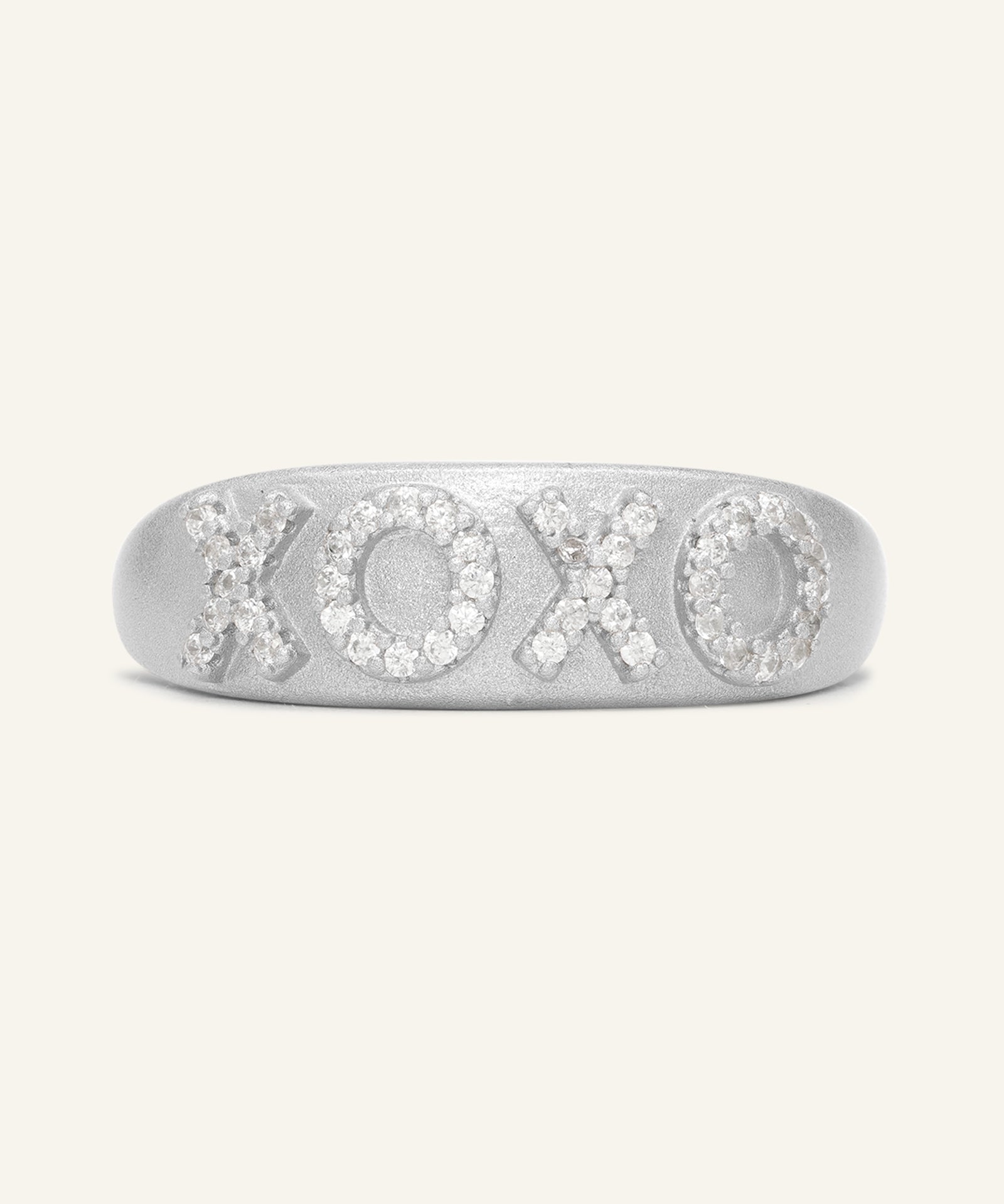 XOXO Ring in silver, resting on a warm linen background