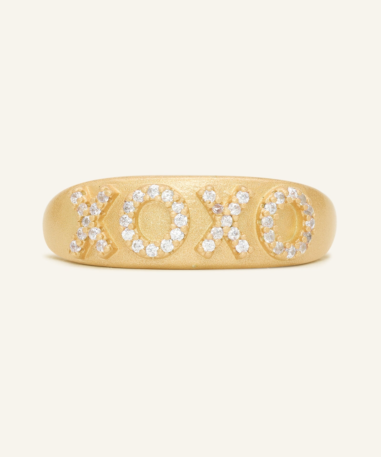 XOXO Ring in yellow gold, resting on a warm linen background