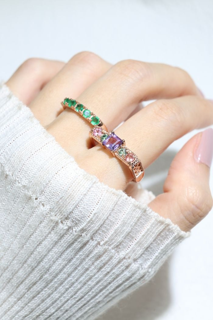Arc de Triomphe Amethyst Ring in rose gold, angled view worn on a hand beside a green gemstone ring