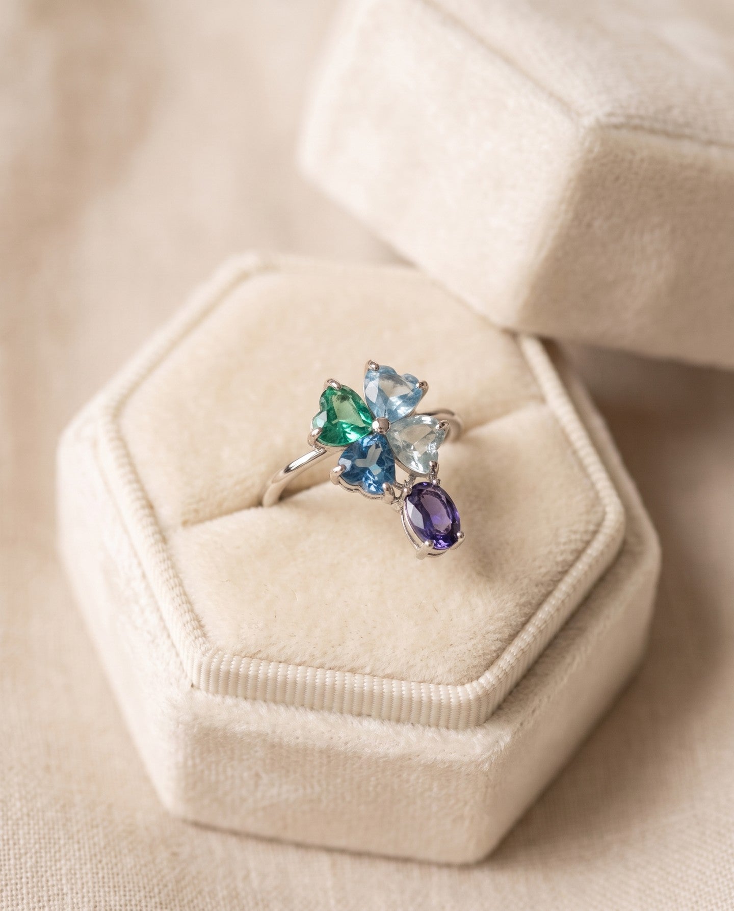 Silver blue topaz clover ring with dangling violet iolite displayed on an ivory jewellery box