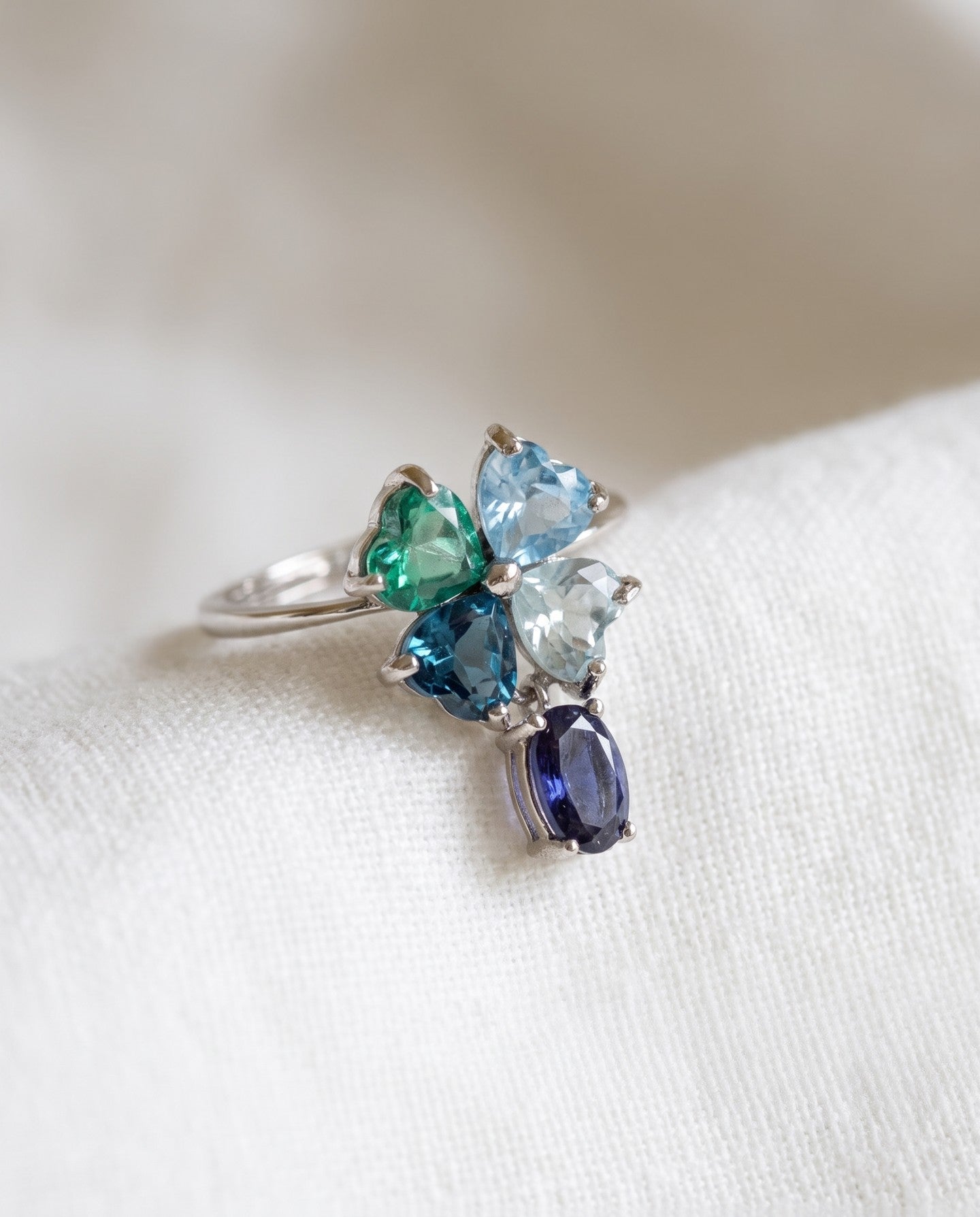 Silver blue topaz clover ring with dangling violet iolite resting on ivory linen