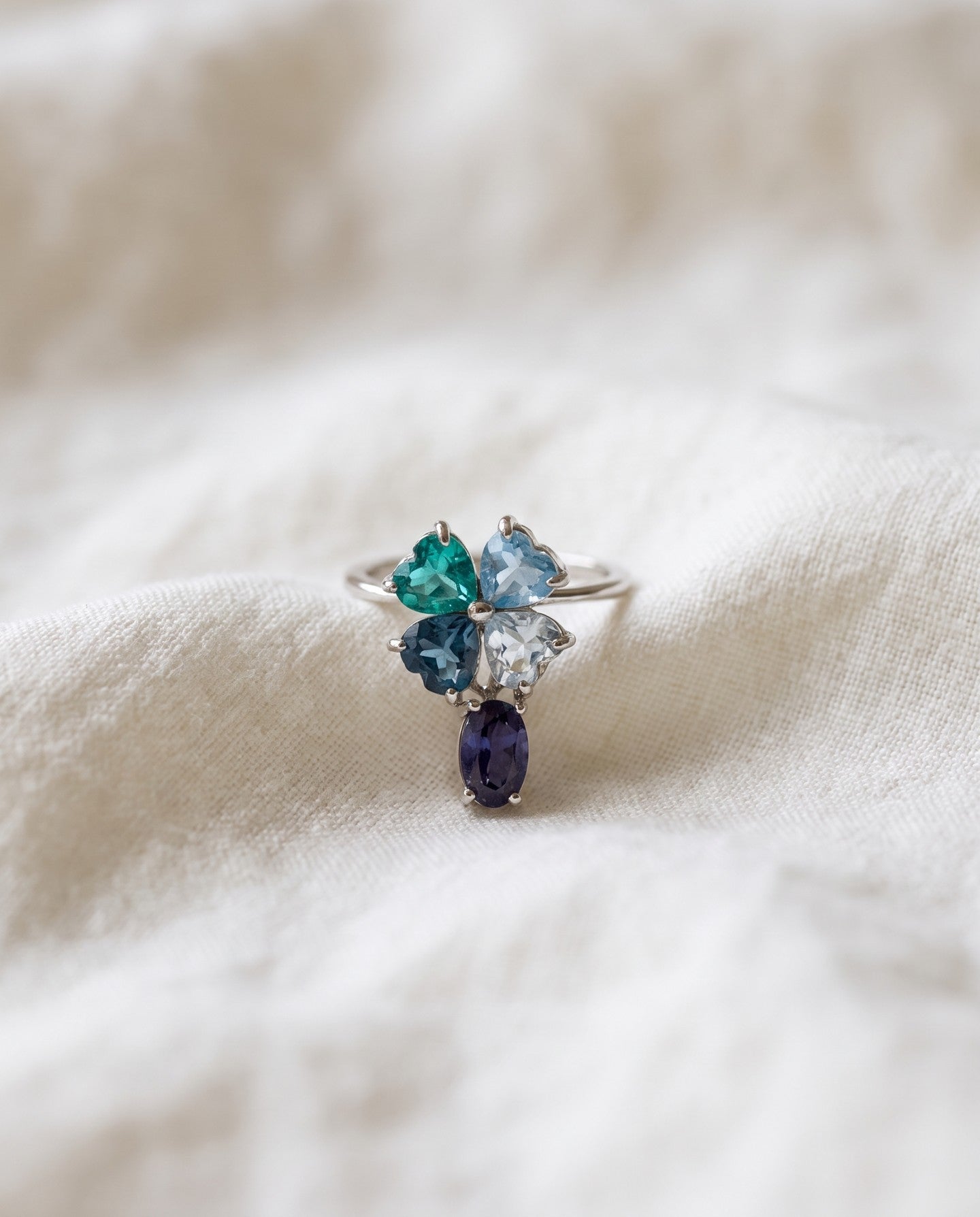 Silver blue topaz clover ring with dangling violet iolite resting on ivory linen