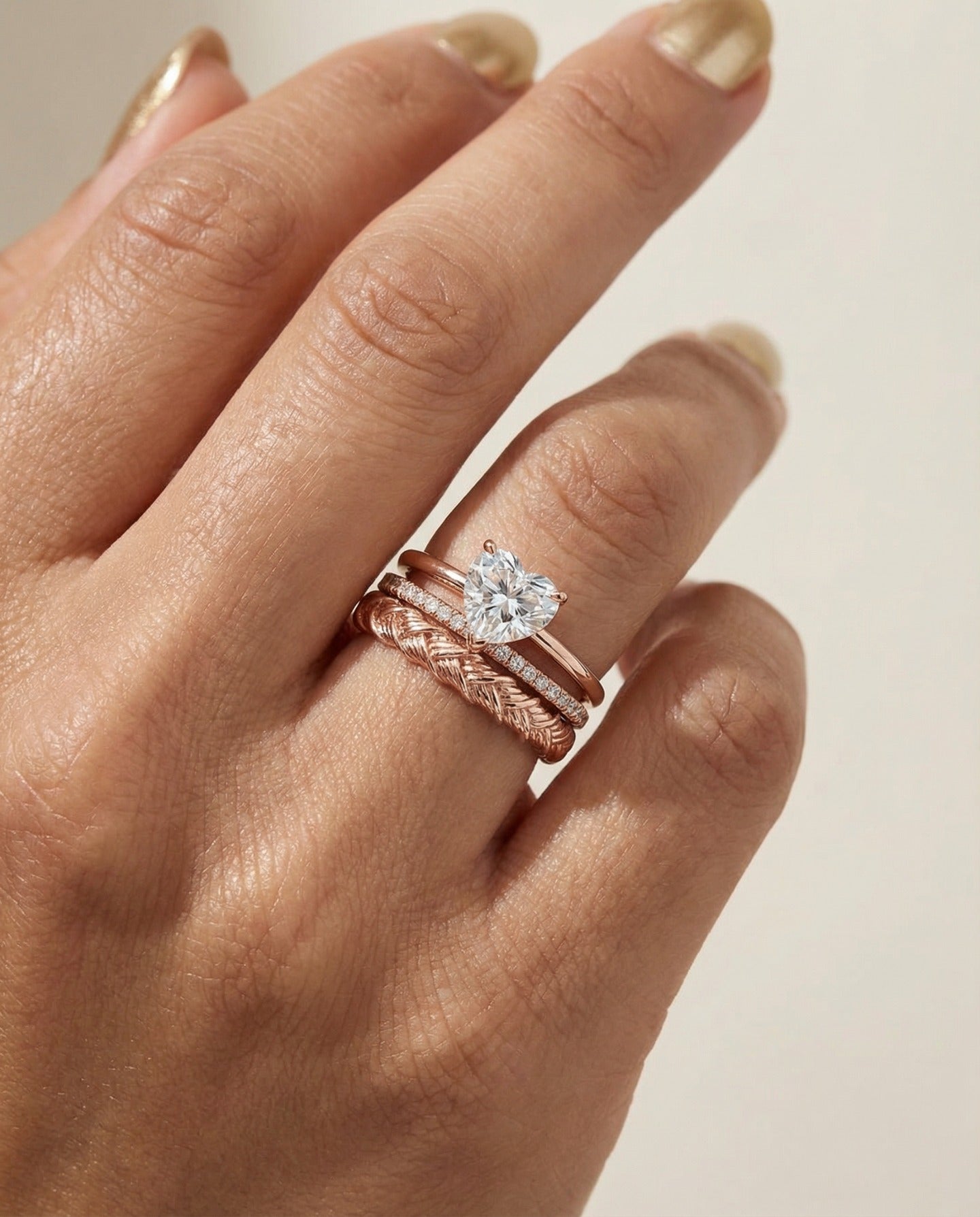 Braided Bliss Band in rose gold, worn beneath a solitaire ring in a close-up hand view