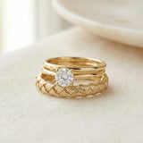 Braided Bliss Band in yellow gold, stacked with a solitaire ring on cream fabric