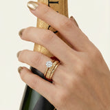 Braided Bliss Band in yellow gold, worn in a ring stack while holding a gold bottle