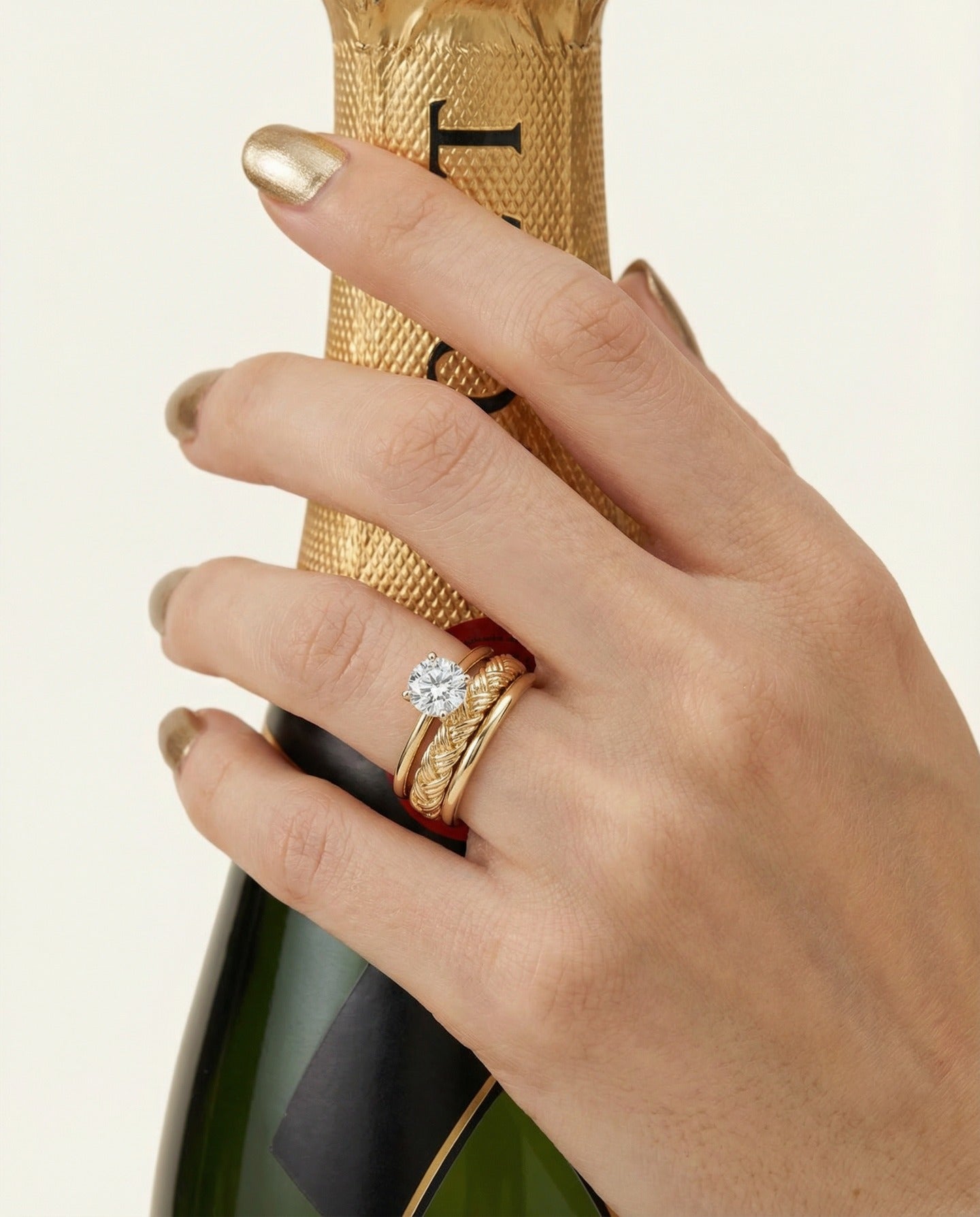 Braided Bliss Band in yellow gold, worn in a ring stack while holding a gold bottle