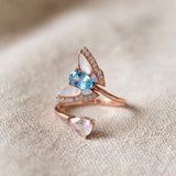 Rose gold butterfly ring with Swiss blue topaz, rose quartz and mother-of-pearl wings resting on textured ivory linen