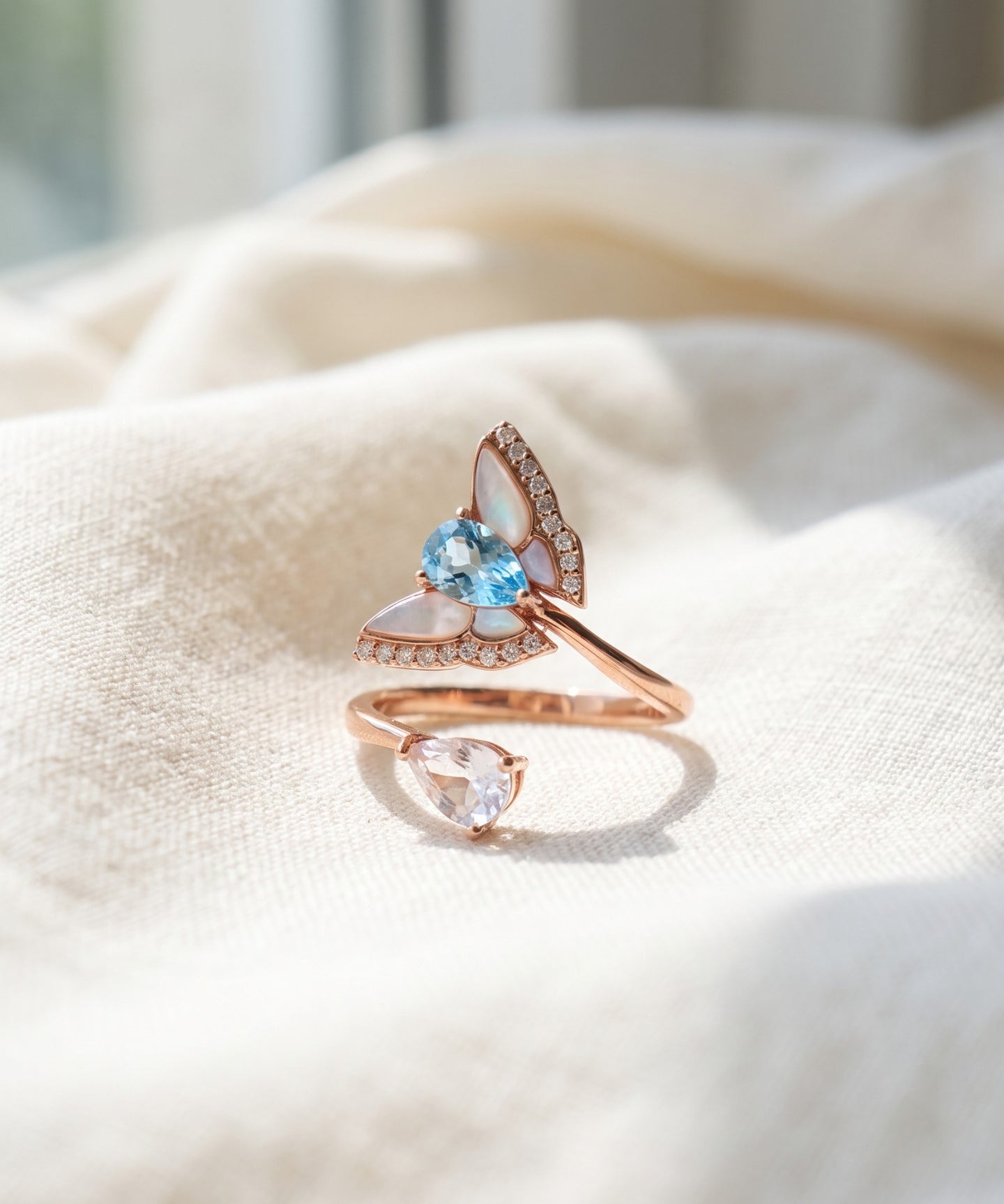 Rose gold butterfly ring with Swiss blue topaz, rose quartz and mother-of-pearl wings on ivory linen