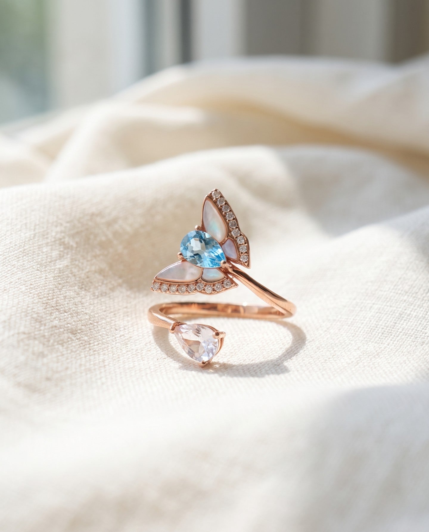 Rose gold butterfly ring with Swiss blue topaz, rose quartz and mother-of-pearl wings on ivory linen