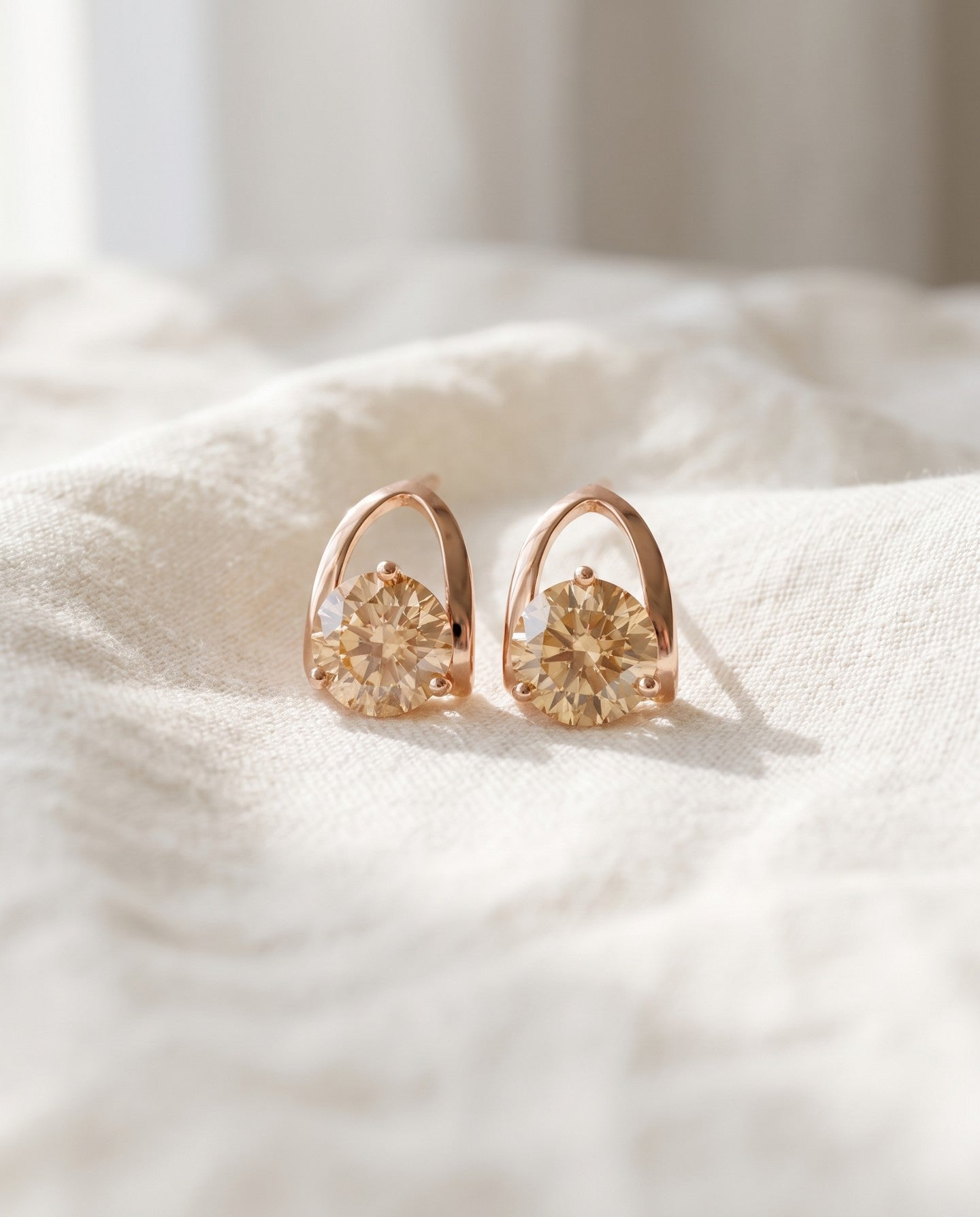 Champagne moissanite stud earrings in rose gold resting on ivory linen