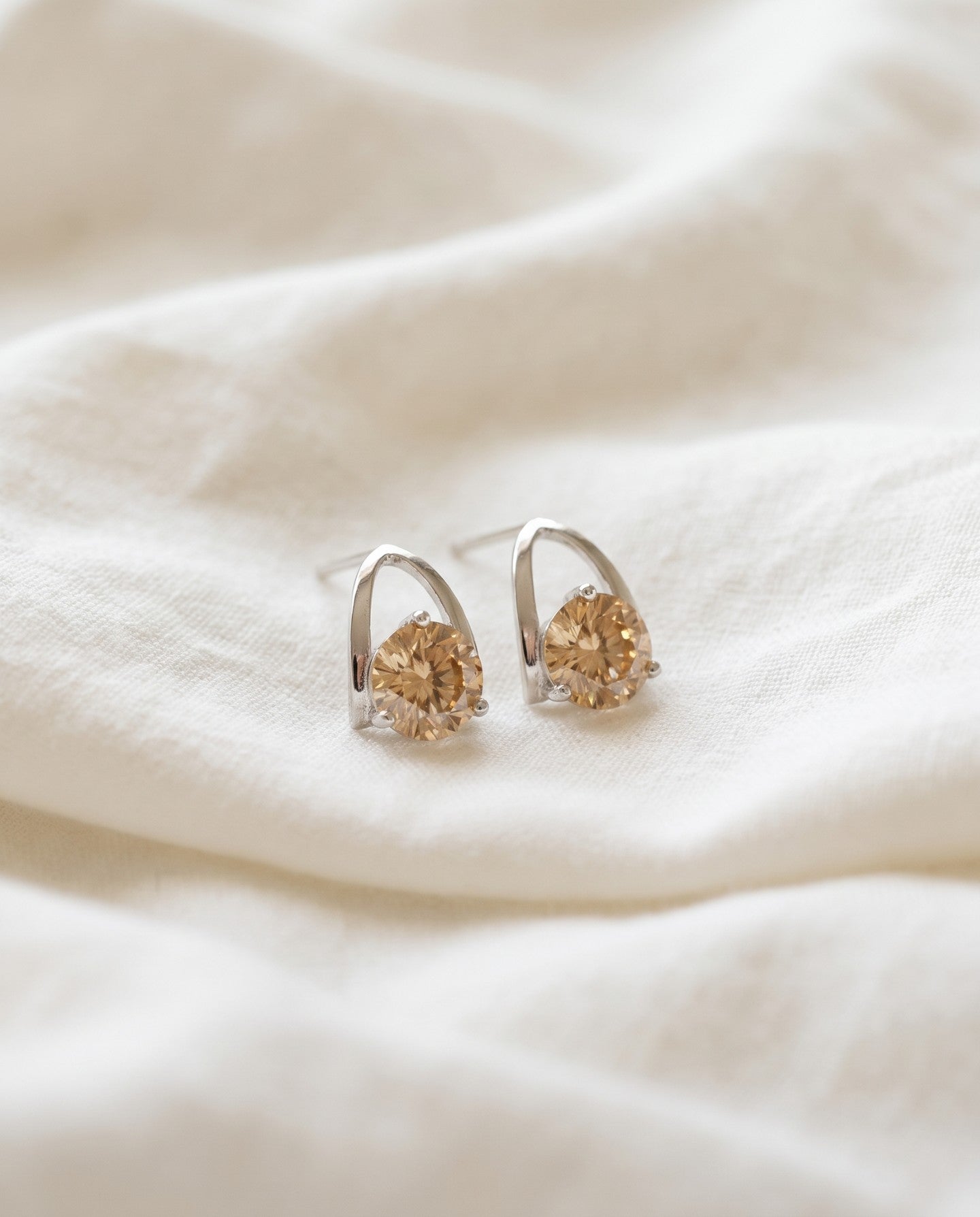 Champagne moissanite stud earrings in silver resting on ivory linen