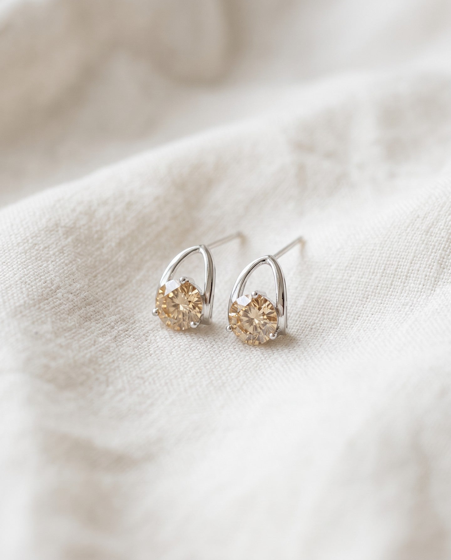 Champagne moissanite stud earrings in silver resting on ivory linen