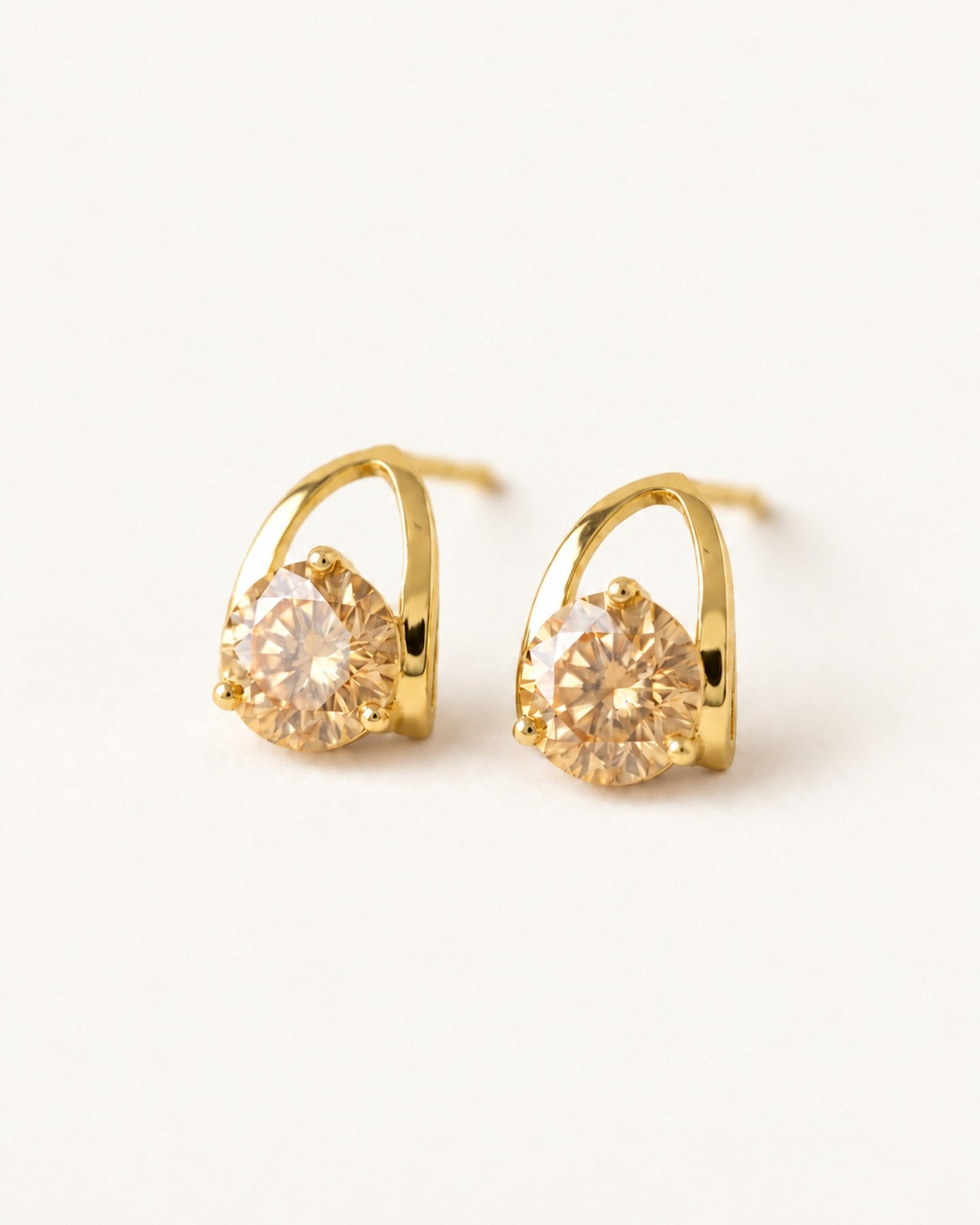 Champagne moissanite stud earrings in yellow gold on an ivory background