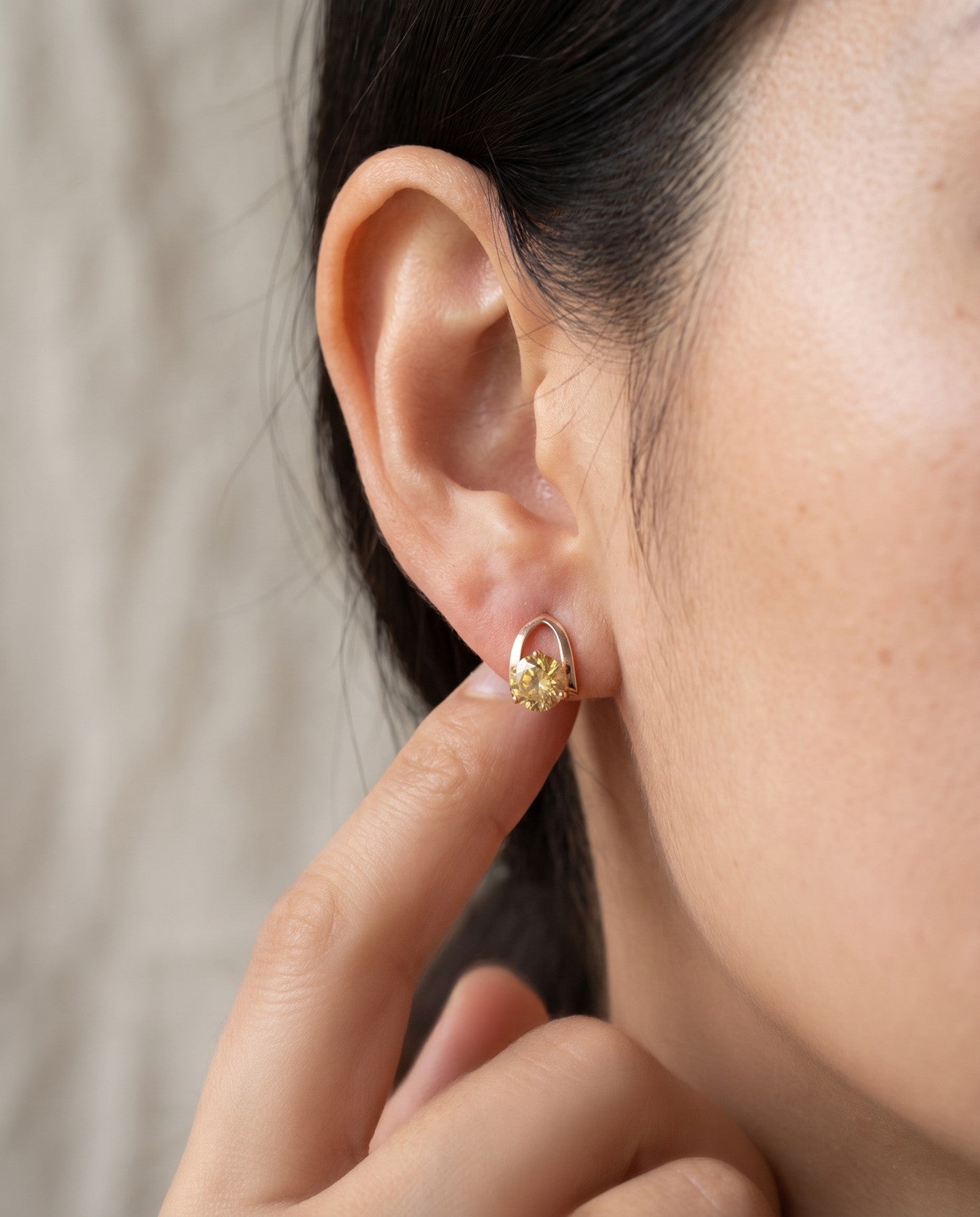 Champagne moissanite stud earrings in yellow gold worn on an ear