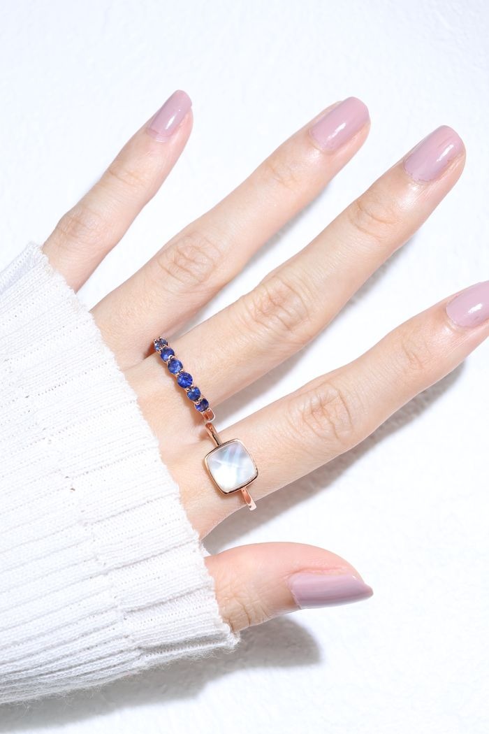 Clear Quartz and Mother of Pearl Sugarloaf Ring in rose gold, worn on an angled hand beside a blue gemstone band