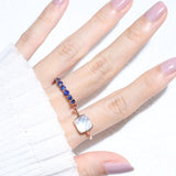 Clear Quartz and Mother of Pearl Sugarloaf Ring in rose gold, worn on an angled hand beside a blue gemstone band