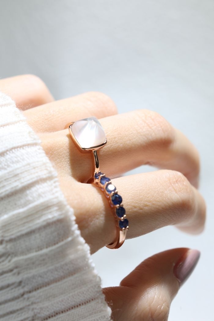 Clear Quartz and Mother of Pearl Sugarloaf Ring in rose gold, side-angle close-up of the ring worn beside a blue gemstone band