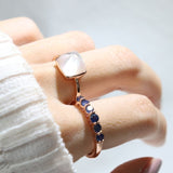 Clear Quartz and Mother of Pearl Sugarloaf Ring in rose gold, side-angle close-up of the ring worn beside a blue gemstone band
