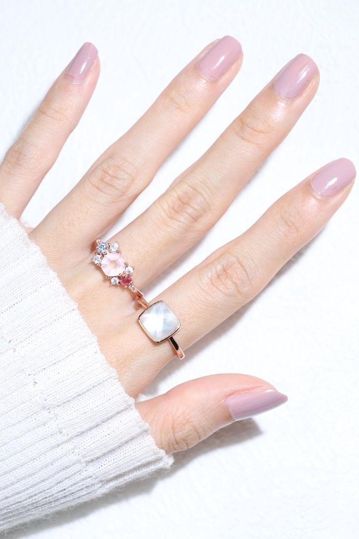 Clear Quartz and Mother of Pearl Sugarloaf Ring in rose gold, worn on a hand with a pink floral ring and white knit sleeve