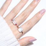 Clear Quartz and Mother of Pearl Sugarloaf Ring in rose gold, worn on a hand with a pink floral ring and white knit sleeve