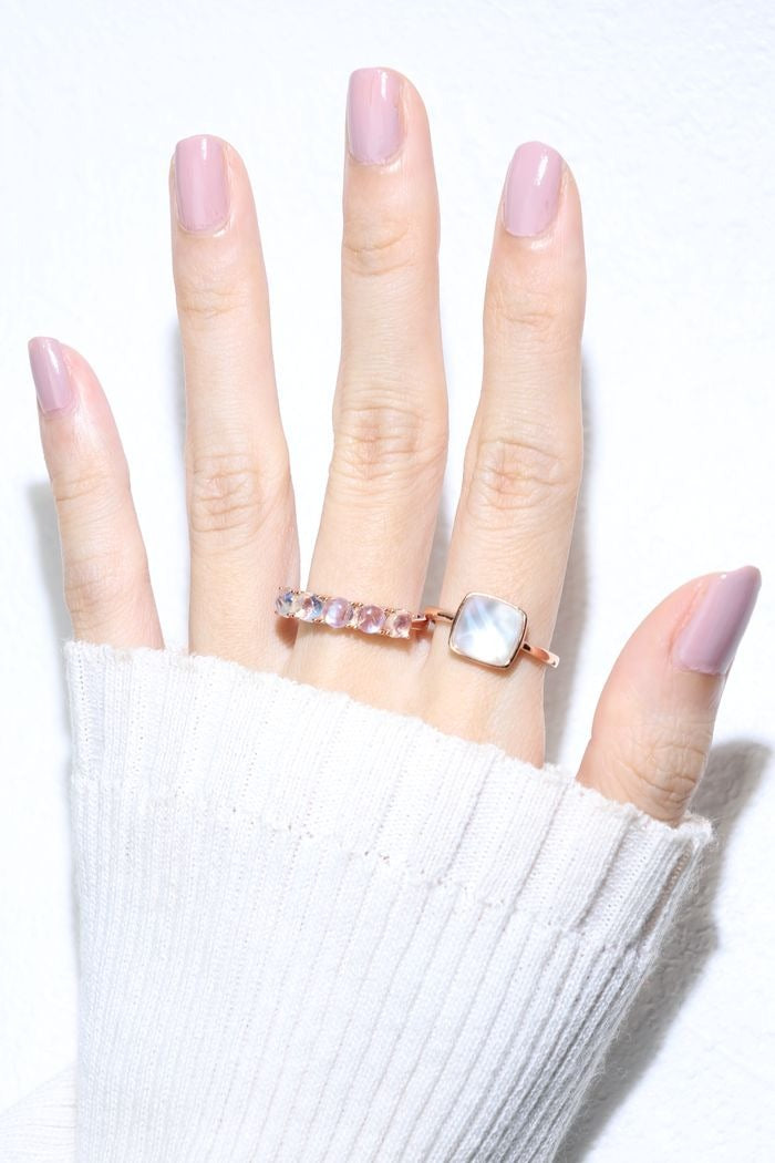 Clear Quartz and Mother of Pearl Sugarloaf Ring in rose gold, worn on a raised hand beside a pink gemstone ring
