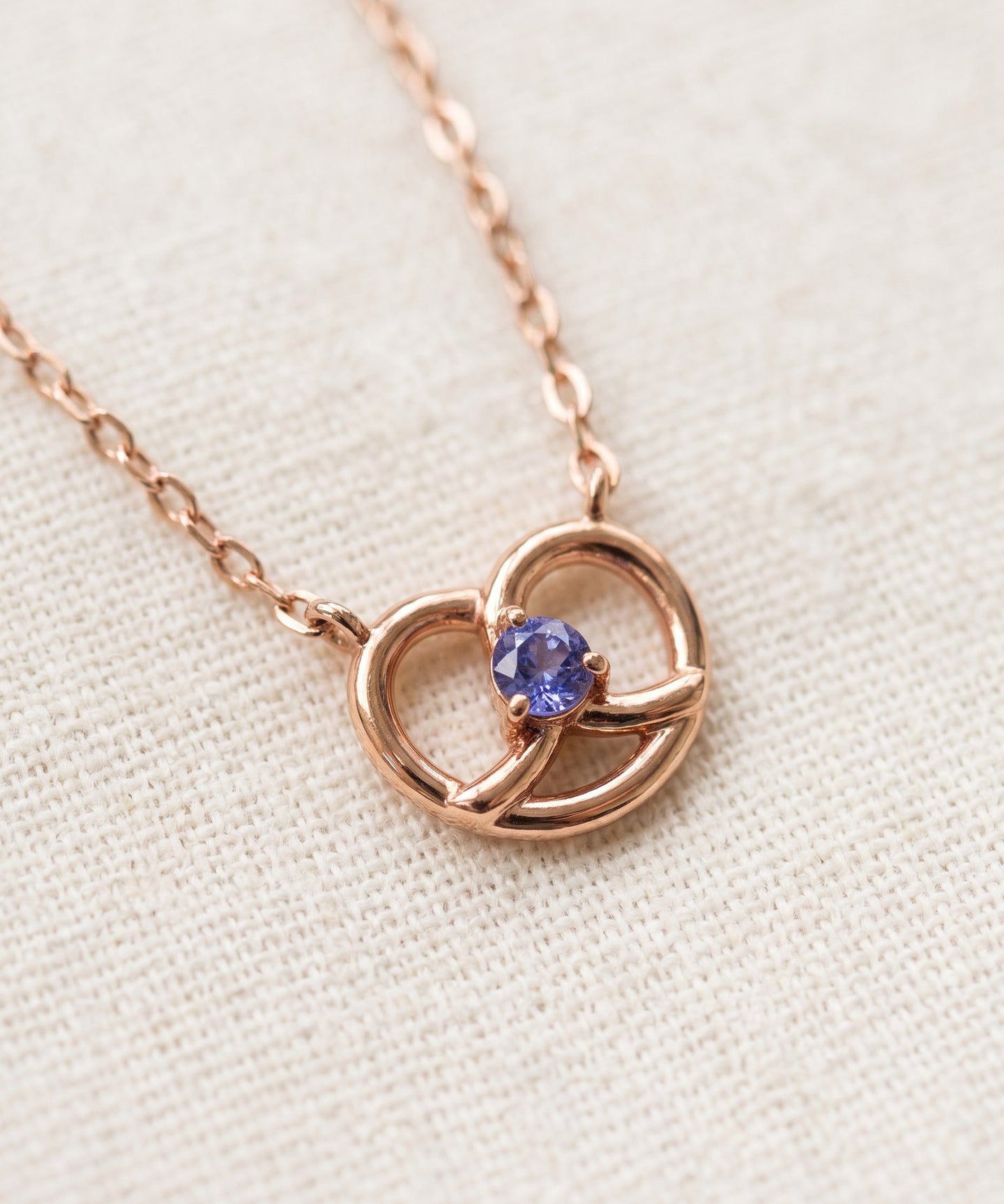 Croissant Heart Tanzanite Necklace in rose gold, close-up of the heart pendant on ivory linen