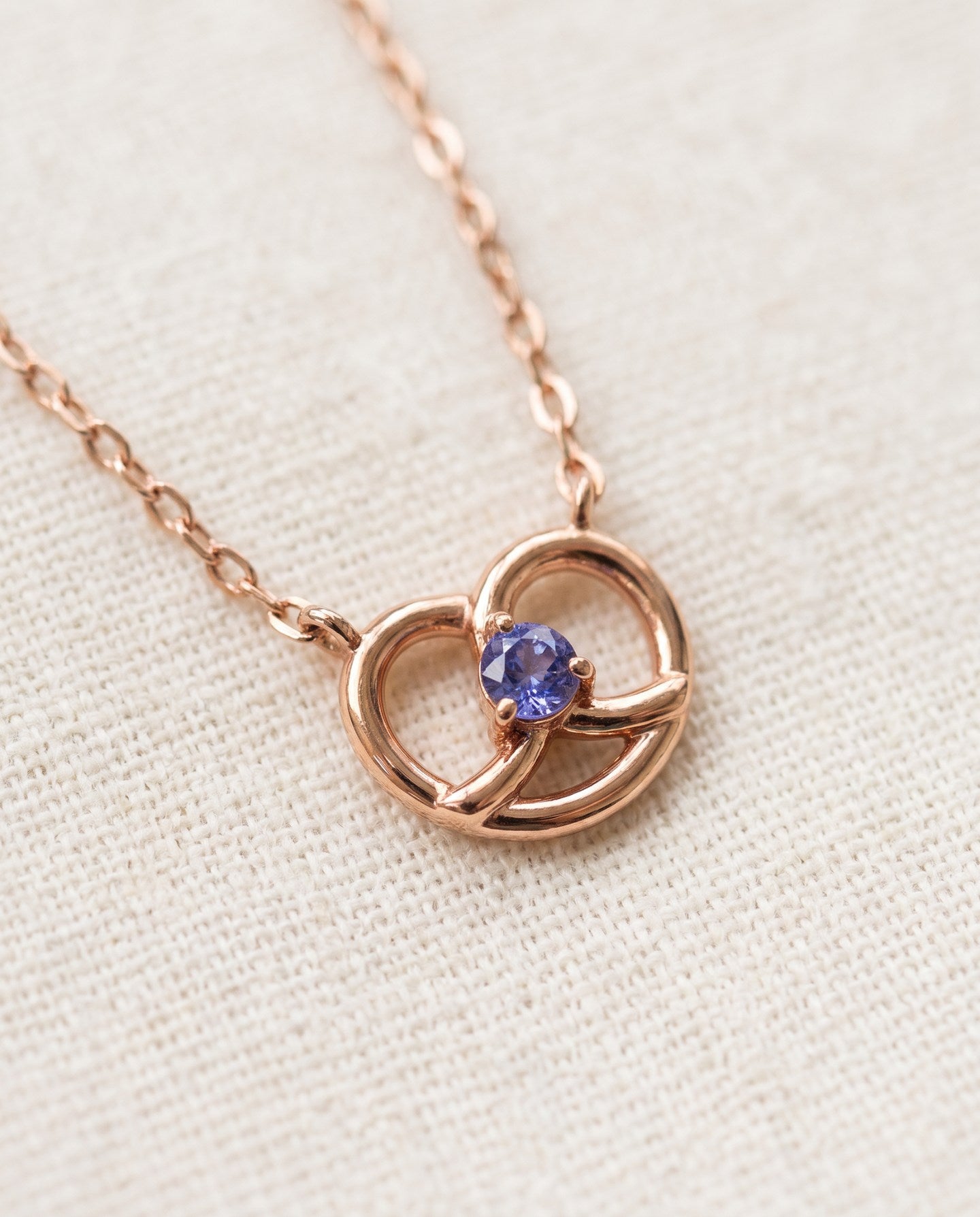 Croissant Heart Tanzanite Necklace in rose gold, close-up of the heart pendant on ivory linen