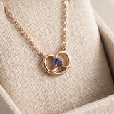 Croissant Heart Tanzanite Necklace in rose gold, displayed upright on a linen jewellery cushion