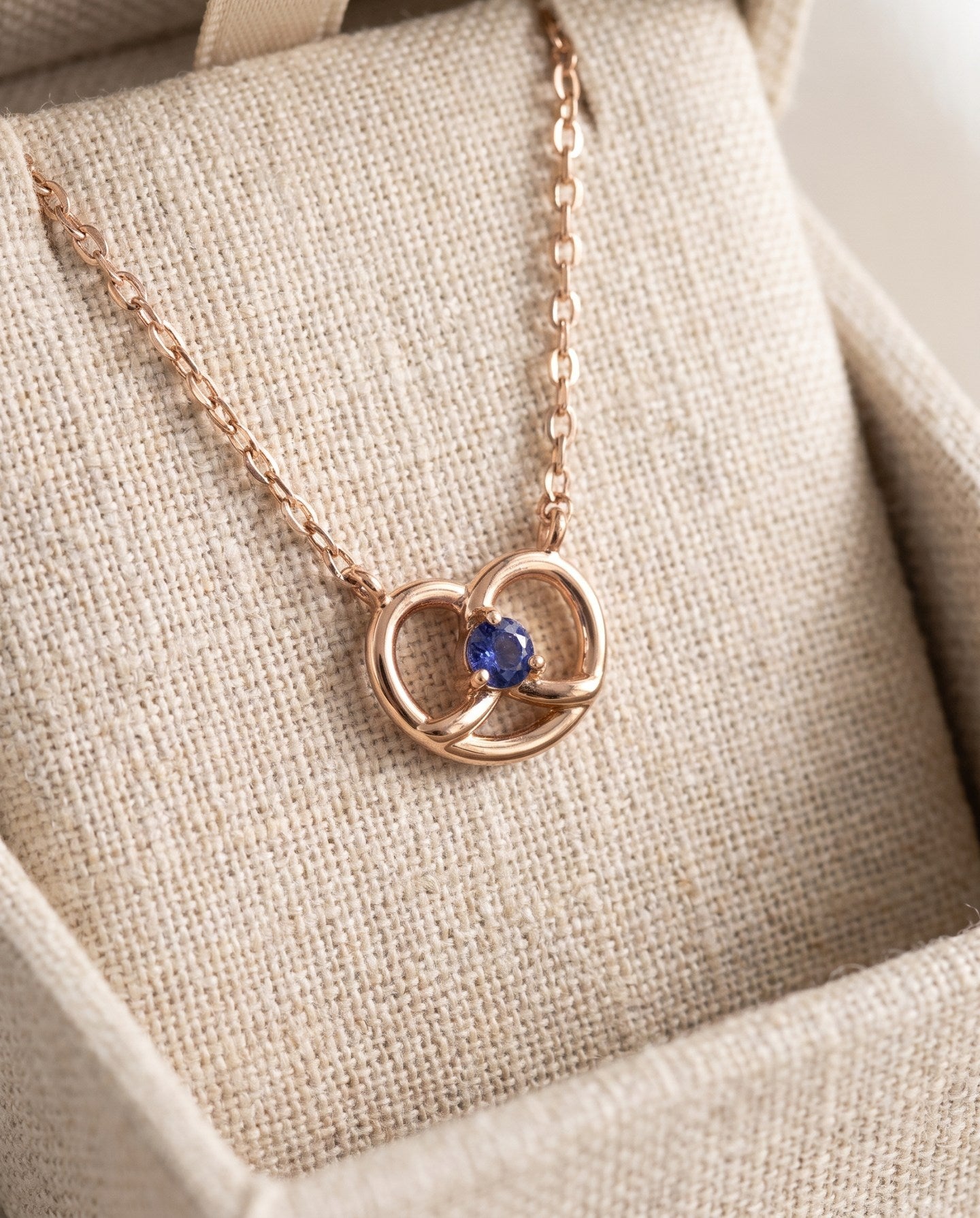 Croissant Heart Tanzanite Necklace in rose gold, displayed upright on a linen jewellery cushion