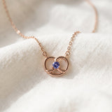 Croissant Heart Tanzanite Necklace in rose gold, arranged with its cable chain on soft ivory fabric